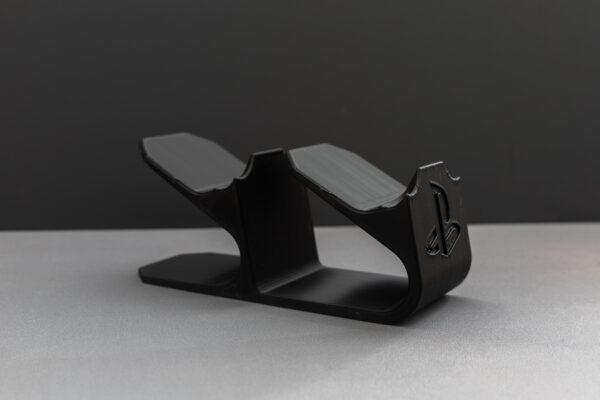 Black 3D printed plastic stand or holder with dual curved sections, showing PlayStation logo, designed to hold gaming controllers.