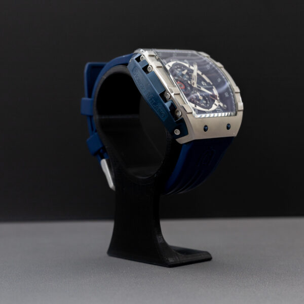 A luxury chronograph watch with blue dial and silver case displayed on a 3D-printed black watch stand with a minimalist curved design.