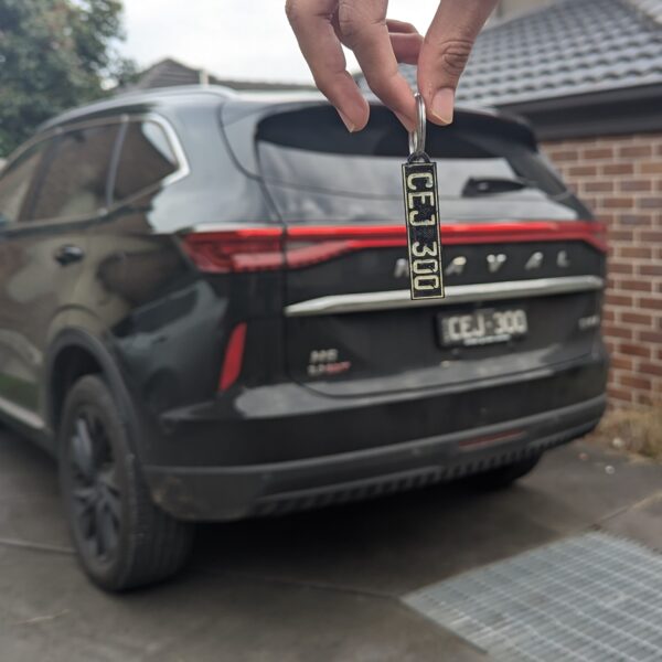 3D Printed Car key charm showing "CEJ 300" in black with white text, held in front of a black SUV with red taillights.